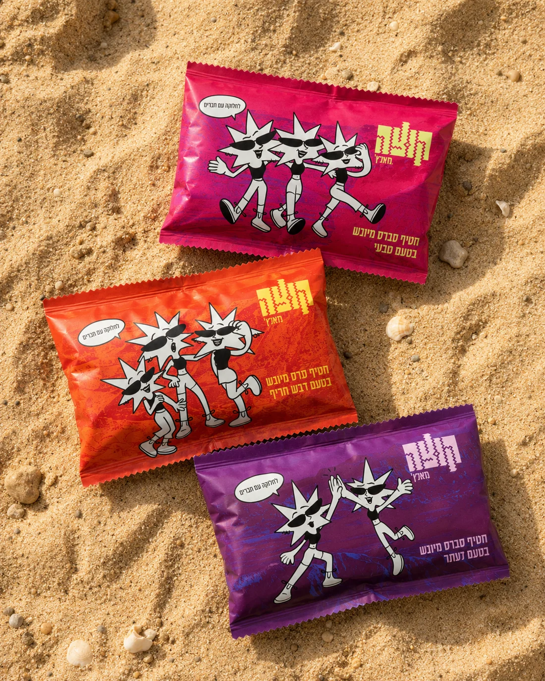 Three Kutza snack bags on sand: magenta, orange and purple, each with the mascot dancing